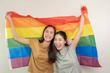 Güzel görünümlü lezbiyen çiftler gökkuşağı bayraklarını parlak bir şekilde örterler. Asyalı genç çift birbirlerine mutlu bir şekilde sarılıyorlar, aşık olan sevgili, biseksüeller, homoseksüellik, özgürlük, ifade, mutlu hayat.