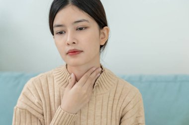 Asyalı kadın boğazı ağrıdığı için boynuna takıldı. Dişi bademcik iltihabı iltihaba neden olur. Su alarak, antibiyotik alarak, doktora, virüse, korona virüsüne, gribe, gribe danışarak tedavi olunur.