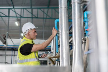 Güvenlik kaskı takan mühendisler veya fabrika yöneticileri üretim hattındaki makineleri inceler. Kamu müfettişi makineyi kontrol et ve standardı karşılamak için sistemi test et. makine, bakım.