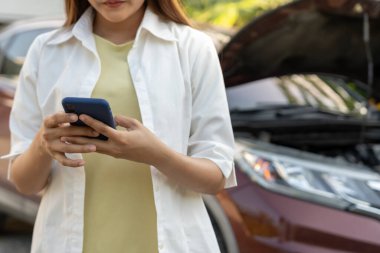 breakdown, broken car, repair. Woman uses mobile phone check insurance premiums through application due to car accident . Find garage to get car fixed during country tour, waiting for help, emergency.
