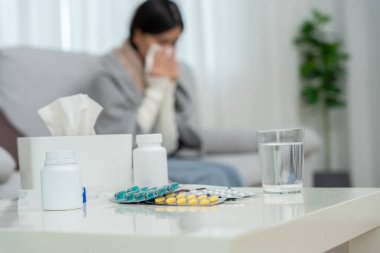 Yüksek ateşi olan genç bir Asyalı kadın vücut ısısını kontrol ederken hapşırıyor ve mevsimsel gribi olan burnu akıyor. İlaç, virüs, koronavirüs, hastalık, solunum, alerji...