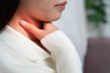 Asyalı kadın boğazı ağrıdığı için boynuna takıldı. Dişi bademcik iltihabı iltihaba neden olur. Su alarak, antibiyotik alarak, doktora, virüse, korona virüsüne, grip virüsüne danışarak,