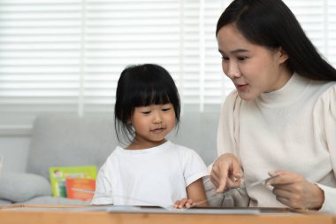 Mutlu Asyalı anne rahatla ve evde bebek zamanlarıyla kitap oku. Ebeveyn kızıyla kanepede oturup masal okuyor. öğrenme, çocuk bakımı, gülme, eğitim, hikaye anlatma, uygulama