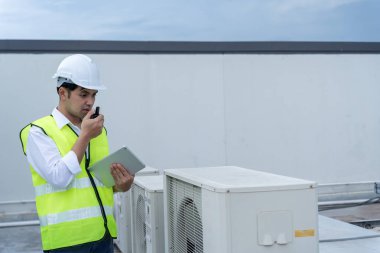 Asyalı bakım mühendisi fabrikanın çatısında çalışıyor. Müteahhit kompresör sistemini denetleyecek ve inşaatta havalandırma sistemi kurmayı planlıyor. teknoloji, çevrimiçi, mobil uygulama.