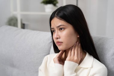 Asyalı kadın boğazı ağrıdığı için boynuna takıldı. Dişi bademcik iltihabı iltihaba neden olur. Su alarak, antibiyotik alarak, doktora, virüse, korona virüsüne, grip virüsüne danışarak,