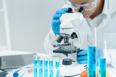 Bilimadamı ileri bilimsel laboratuvarda biyokimyasal örnekleri analiz ediyor. Tıbbi profesyonel kullanım mikroskobu virüsün mikrobiyolojik gelişimini gösteriyor. Fen laboratuvarında biyoteknoloji araştırması