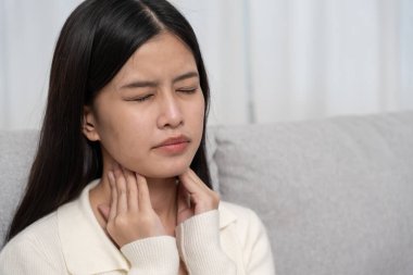 Asyalı kadın boğazı ağrıdığı için boynuna takıldı. Dişi bademcik iltihabı iltihaba neden olur. Su alarak, antibiyotik alarak, doktora, virüse, korona virüsüne, gribe, gribe danışarak tedavi olunur.