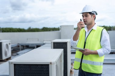 Asyalı bakım mühendisi fabrikanın çatısında çalışıyor. Müteahhit kompresör sistemini denetleyecek ve inşaatta havalandırma sistemi kurmayı planlıyor. teknoloji, çevrimiçi, mobil uygulama
