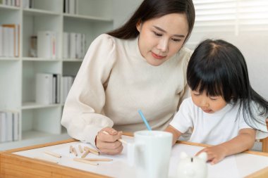 Mutlu Asyalı anne küçük kız için boya öğreniyor. Komik aile evde mutlu ve heyecanlı. Anne ve kızı birlikte vakit geçiriyorlar. Tatil, Etkinlik