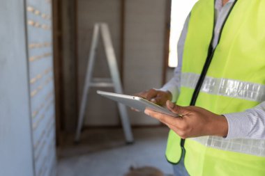 Müfettiş ya da mühendis, tablet kullanarak yeni ev inşaatını ve kalite güvencesini denetliyor. Mühendisler, mimarlar ya da irtibat görevlileri ev sahiplerine devretmeden önce evi inşa etmek için çalışıyorlar.