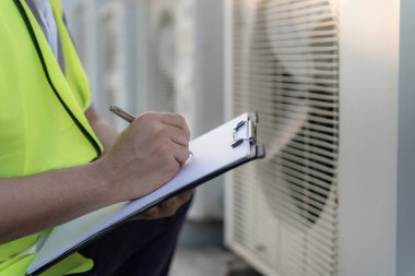 Asyalı bakım mühendisi fabrikanın çatısında çalışıyor. Müteahhit kompresör sistemini denetleyecek ve inşaatta havalandırma sistemi kurmayı planlıyor. Kontrol listesi, müfettiş, kontrol