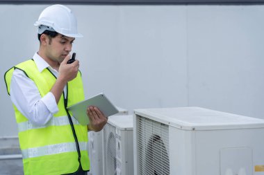 Asyalı bakım mühendisi fabrikanın çatısında çalışıyor. Müteahhit kompresör sistemini denetleyecek ve inşaatta havalandırma sistemi kurmayı planlıyor. teknoloji, çevrimiçi, mobil uygulama.