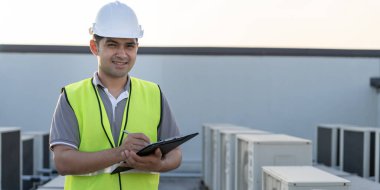 Asyalı bakım mühendisi portresi fabrikanın çatısında çalışıyor. Müteahhit kompresör sistemini denetleyecek ve inşaatta havalandırma sistemi kurmayı planlıyor. teknoloji