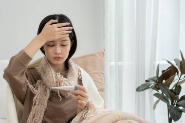 Young Asian woman having high fever while checking body temperature, female sneezing and runny nose with seasonal influenza, allergic, digital thermometer, virus, coronavirus, illness, respiratory