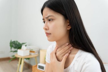 Asyalı kadın boğazı ağrıdığı için boynuna takıldı. Dişi bademcik iltihabı iltihaba neden olur. Su alarak, antibiyotik alarak, doktora, virüse, korona virüsüne, grip virüsüne danışarak,