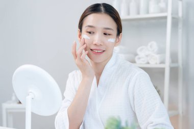 Güzel bir kadın aynanın önünde oturur. Krem sürerek makyaj yapan sağlıklı bir kadın yüzü. Cilt kremi reklamı, kırışıklık önleyici, bebek yüzü, beyazlatma, nemlendirici, gözenekleri sıkılaştırma serumu.