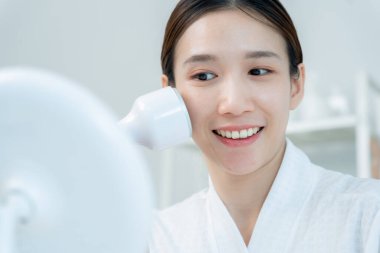 Güzel Asyalı kadınlar gözeneklerini sıkmak için aletler kullanır. Sağlıklı yüzler. Yüz bakımı ve tedavisi. Deri reklamı. Yüz kremi, kırışıklık önleyici, bebek yüzü, beyazlatma, nemlendirici, gözenek sıkılaştırıcı serum.