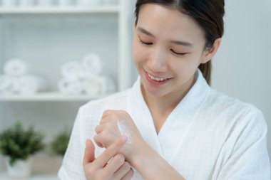 Güzel Asyalı kadın gülümsüyor, cilt kremi kullanıyor. Sağlıklı bir kadın vücuduna krem sürer. Cilt kremi reklamı, kırışıklık önleyici, bebek yüzü, beyazlatma, nemlendirici, gözenekleri sıkılaştırma serumu.