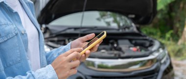 breakdown, broken car, repair. Woman uses mobile phone check insurance premiums through application due to car accident . Find garage to get car fixed during country tour, waiting for help, emergency.