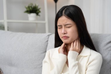 Asyalı kadın boğazı ağrıdığı için boynuna takıldı. Dişi bademcik iltihabı iltihaba neden olur. Su alarak, antibiyotik alarak, doktora, virüse, korona virüsüne, gribe, gribe danışarak tedavi olunur.