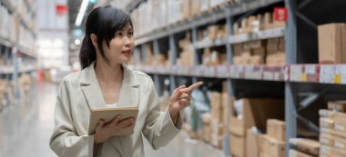 Dijital tablet kullanan bir iş kadını, dağıtım deposu fabrikasında stok ürün envanterini kontrol ediyor. Lojistik ticaret nakliyesi ve teslimatı..