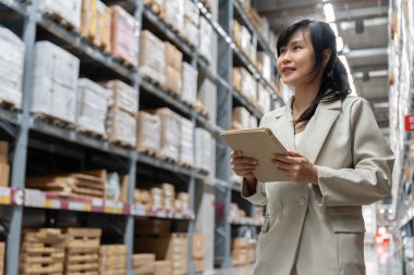Asyalı kadın işyeri sahibi dijital tablet kullanıyor dağıtım deposu fabrikasındaki stok ürün envanterini kontrol ediyor. Lojistik iş gemisi ve teslimatı, envanter akışı, profesyonel iş akışı..