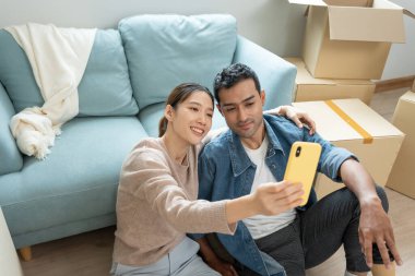 Taşınmak, taşınmak. Aile gülümsemesi ve yeni eve taşındıktan sonra fotoğraf çektirmek. Odanın içinde kişisel eşyalar ve mobilyalar bulunan bir karton kutu vardı. Yeni daireye taşın, apartman dairesi.