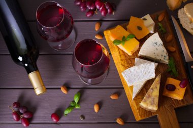 Bardaklar ve bir şişe kırmızı şarap ve şarap aperatifler peynir, ekmek ve fındık kahverengi ahşap arka planda. Yukarıdan bak, en iyi stüdyo çekimi.