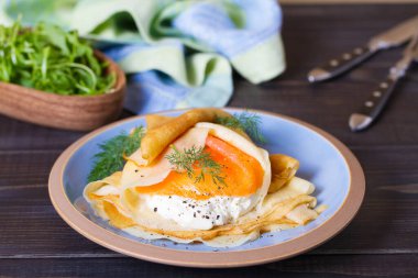 Doldurulmuş ince krep füme somon, krem peynir ve çırpılmış yumurta ve somon. Mavi tabakta krepler