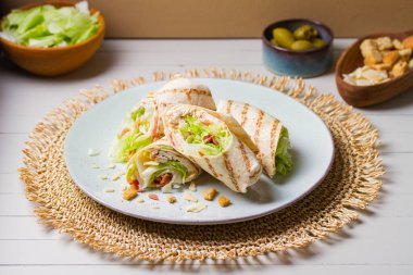 Tavuklu domuz pastırması. Tavuk göğsü fileto, açık ahşap arka planda yeşil tabağa sarılır.