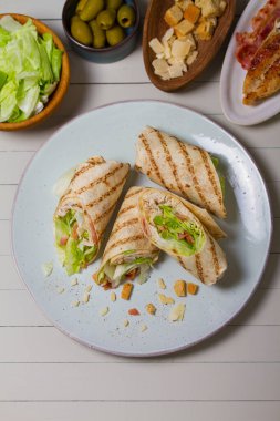 Chicken bacon caeser wrap. Chicken breast fillet wraps on green plate on light wooden background. View from above, top view clipart