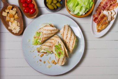 Chicken bacon caeser wrap. Chicken breast fillet wraps on green plate on light wooden background. View from above, top view clipart