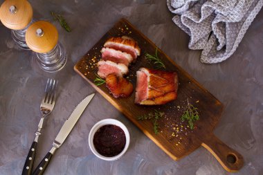 Tahtada kızarmış ördek göğsü filetosu ve gri arka planda kızılcık sosu. Yüksek açı görünümü 