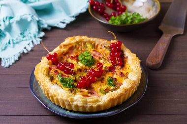 Pastırmalı kiş, kremalı peynir ve kahverengi ahşap arka planda mavi tabakta sebze.