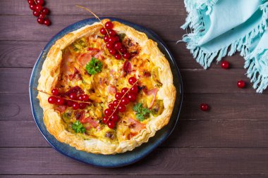 İçinde jambon parçaları, kremalı peynir ve kahverengi ahşap arka planda mavi tabakta sebzeler olan kiş. Yukarıdan görüntüle, en üstten