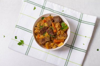 Beyaz arka planda beyaz bir kasede sebzeli leziz biftek güveci. Yüksek açı görünümü