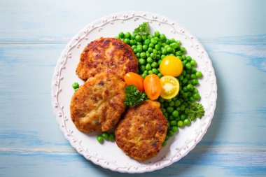 Beyaz tabakta sebzeli balık burgeri. Balık köftesi ya da kek. Yüksek açı görünümü