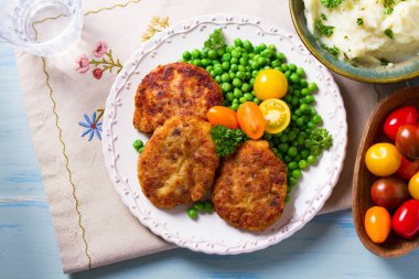 Beyaz tabakta sebzeli balık burgeri. Balık köftesi ya da kek. Yüksek açı görünümü