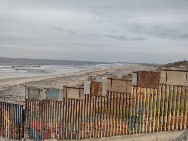 Gloomy View of Rusty Protective Border Wall Mexico Tijuana and United States of America. Defense Against Illegal Immigration, Narcotics, Drugs, Illegal Substances Trafficking due to Cartel Activity. clipart