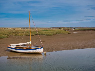 Kuzey Norfolk kıyısındaki bir kanala demirlemiş boş bir tekne. Güneşli bir günde, bulutlu ve mavi bir gökyüzünde çekildi..