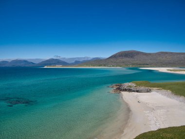 Luskentyre Körfezi 'ndeki Luskentyre Körfezi' nde, İskoçya 'nın dış Hebrides adasının kıyısında iki uzak insan. Güneş ışığı, mavi gökyüzü ve turkuaz suyla.