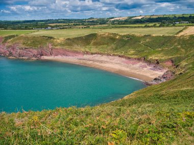 Pembrokeshire, Galler 'deki terk edilmiş Swanlake Sahili' nin kırmızı kumu. Yazın güneşli bir günde, turkuaz bir denizle sahil yolundan alındı..