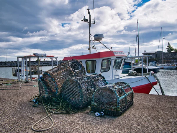 Kuzey İrlanda, İngiltere 'nin Antrim ilçesindeki Carrickfergus kıyı kasabasında kırmızı ve beyaz bir balıkçı teknesinin yanındaki rıhtıma istiridye saksıları (creels) yığıldı..