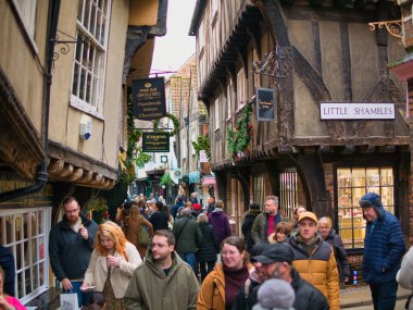 York, UK - Nov 23 2021: Tourists and shoppers in the Shambles area of the City of York in northern England. On the side of an old timbered building, the road sign of the old street of Little Shambles. clipart