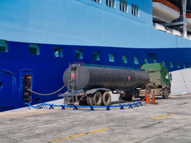 Bridgetown, Barbados - 28 Ocak 2024: Bir karayolu tankeri Bridgetown, Barbados limanına demirlemiş bir yolcu gemisinden atık petrol topluyor. Ön planda mavi bir boru bir su vanasına bağlanıyor..