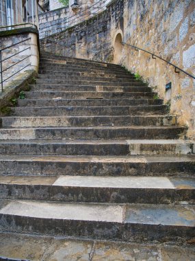 Sağında siyah metal bir tırabzan olan ıslak, gri, açık hava taş basamaklarından dik bir uçuşa bakıyorum. Fransa 'nın Dordogne bölgesinde Rocamadour' da çekildi..