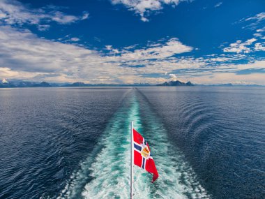 Bodo, Norveç - 18 Haziran 2024: Havila Pollux 'un güneşli bir yaz gününde kıyı kenti Bodo' dan ayrılması. Bayrağın üzerinde Norveç posta servisinin eski logosu var..