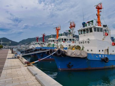 Japonya 'nın Kyushu limanındaki Nagasaki limanına yanaşan römorkörlerin arka planında dağlar ve yukarıda bulutlu bir gökyüzü vardı..