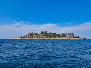 Gunkanjima Adası, Japonya 'nın Nagasaki yakınlarındaki Battleship Adası olarak da bilinir. Terk edilmiş binalar ve kalıntılar berrak mavi gökyüzüne ve sakin denize karşı görünür..