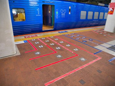 Japonya, Kyushu 'daki tren platformları farklı trenler için yolcu kuyruğu alanlarını gösteriyor. Arka planda açık kapısı olan mavi tren.